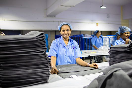 Factory workers sort and fold materials, smiling.